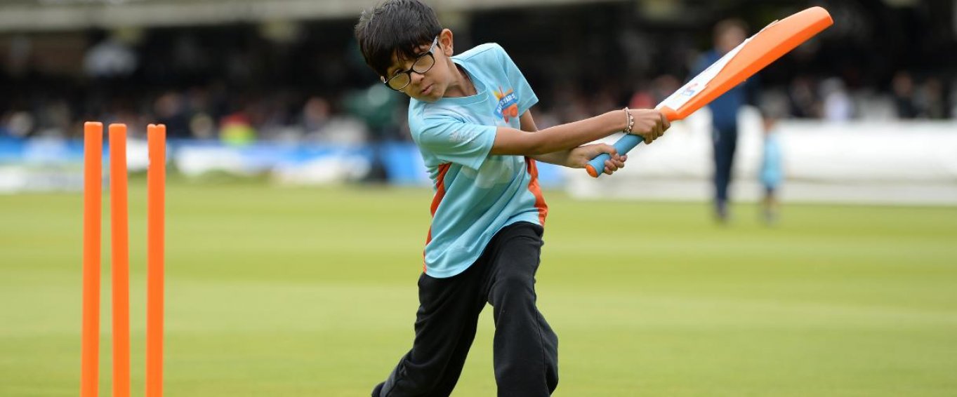 Young Boy in Glasses Swinging a Bat on a Cricket Field