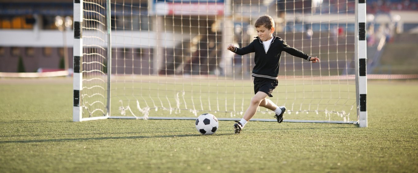 Young Boy Standing in Goal & Kicking a Football