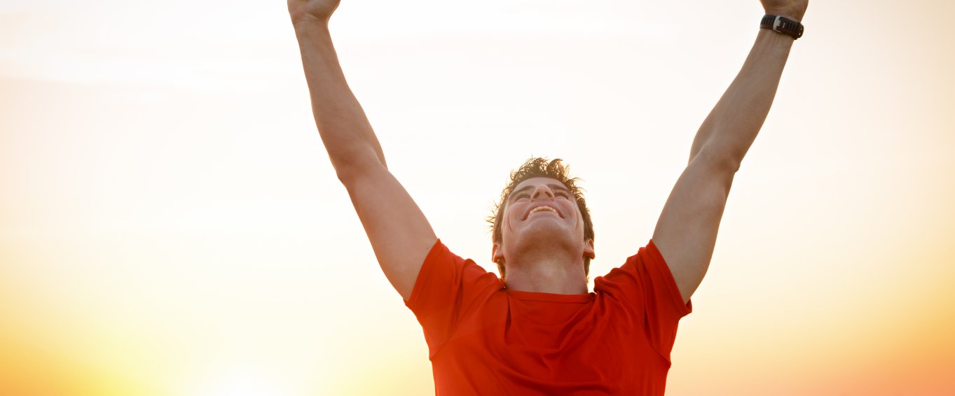 Man in red t shirt celebrating with his arms in the air in front of sunset