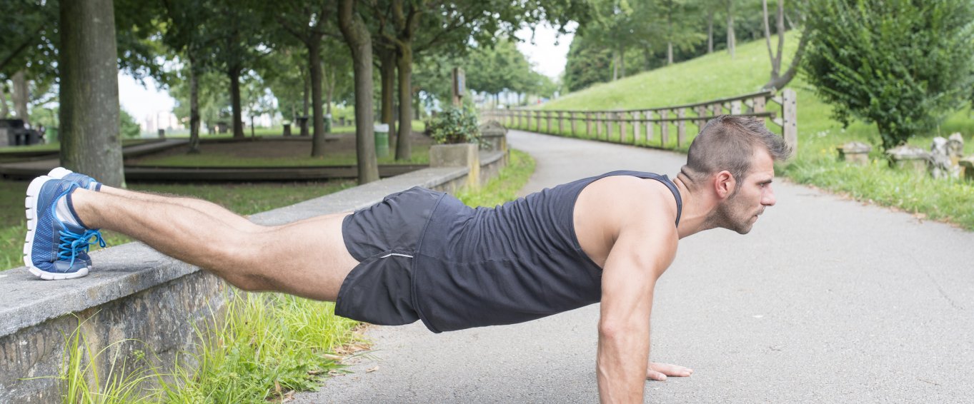 Man doing press up exercise on concrete path near green trees