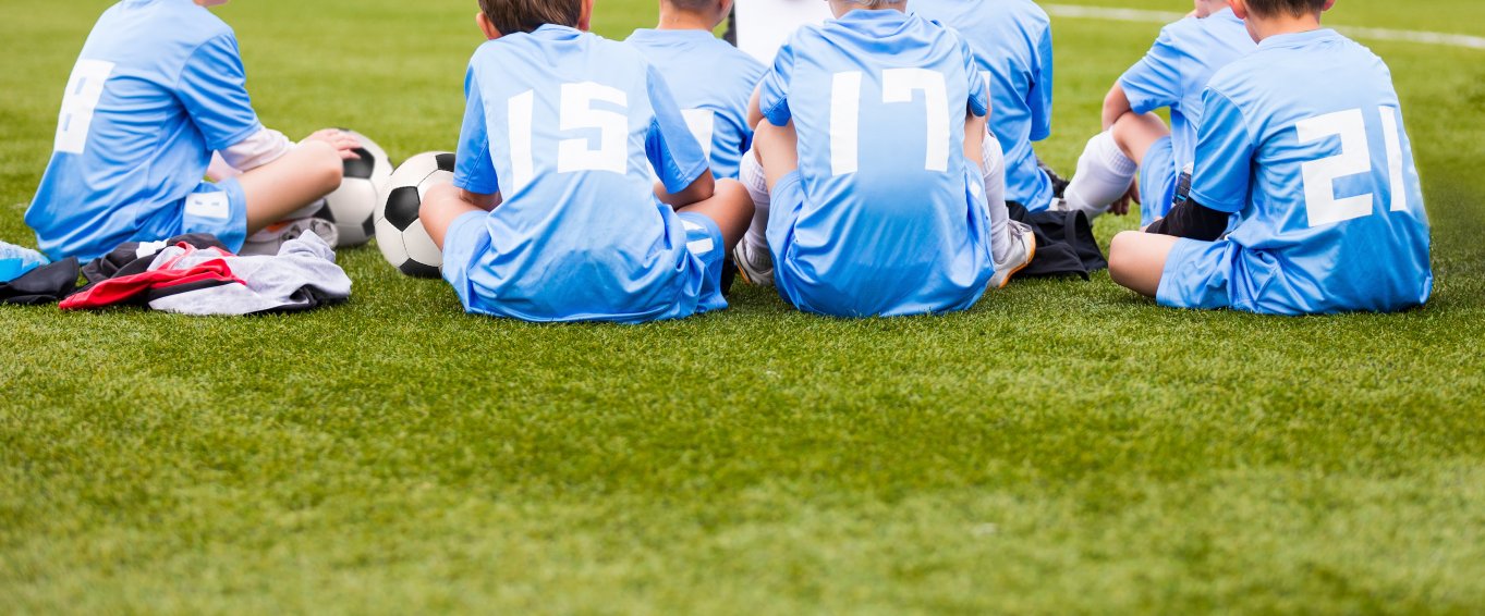 7 Young Boys Sat on the Grass in their Football Kit 