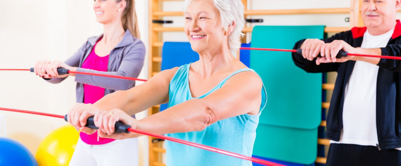 Group of older people and young girl exercising with barbell in gym