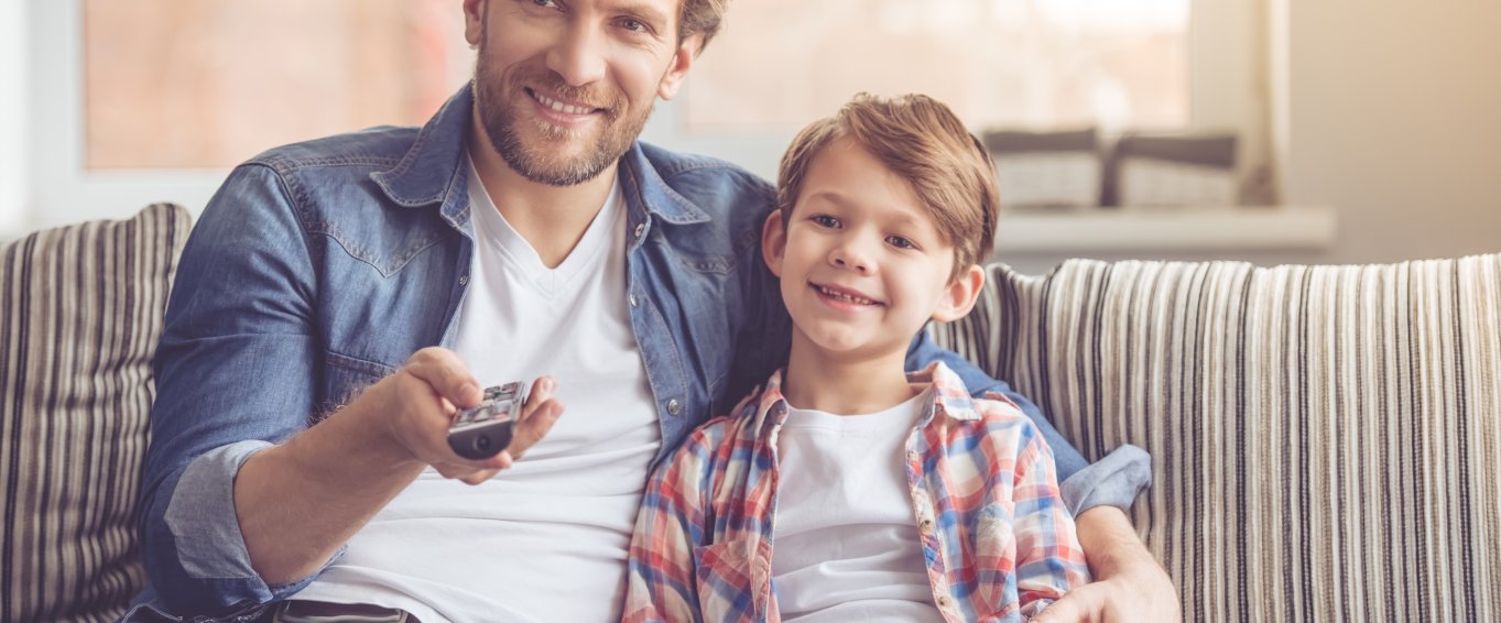 Man and child sat on sofa watching tv