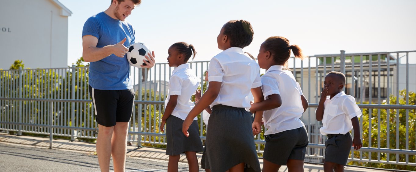 Teacher stood with group of girls and football Teacher stood with group of girls and football
