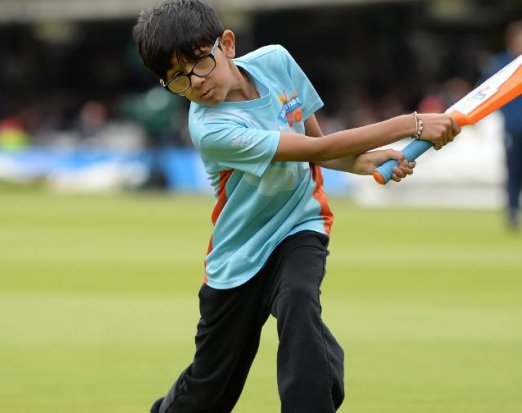 Young Boy in Glasses Swinging a Bat on a Cricket Field