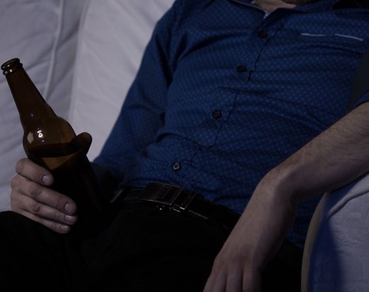 Overweight man sitting on the couch drinking a beer