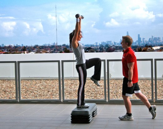 Woman lifting weight on a beach with a personal trainer