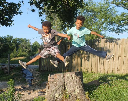 Two Young Boys Leaping Off a Tree Stump