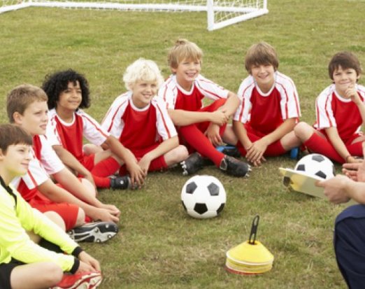 Kids football team sat around a football