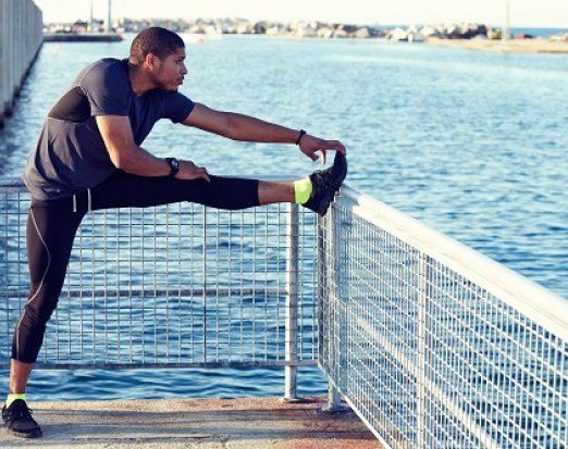 Man stretching leg after run by some water
