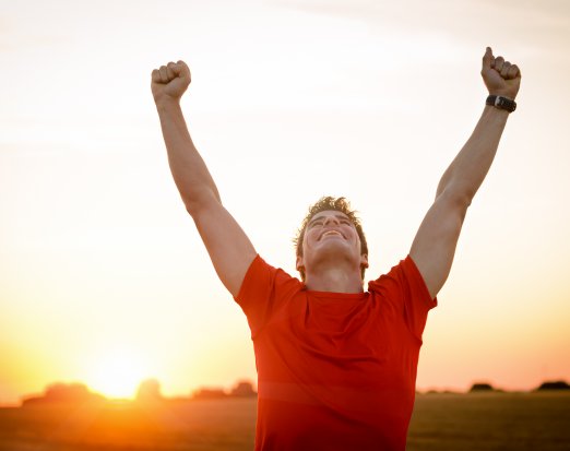 Man in red t shirt celebrating with his arms in the air in front of sunset