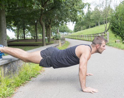 Man doing press up exercise on concrete path near green trees