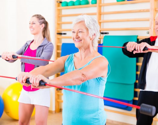 Group of older people and young girl exercising with barbell in gym
