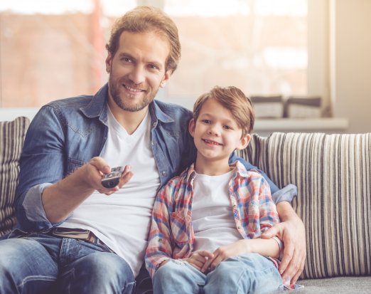 Man and child sat on sofa watching tv