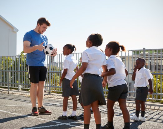 Teacher stood with group of girls and football
