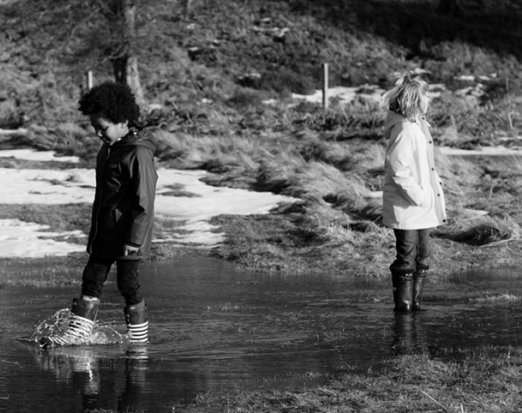 Two Children in Winter Clothes Splashing In a Stream