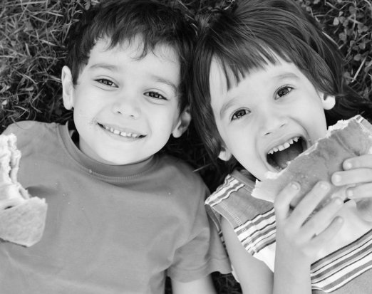 Two Children Lying on Grass & Eating Sandwiches 