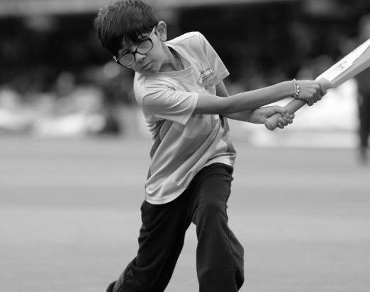 Young Boy in Glasses Swinging a Bat on a Cricket Field