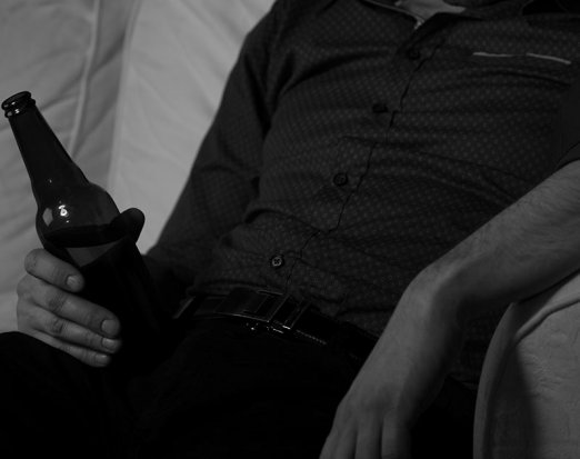 Overweight man sitting on the couch drinking a beer