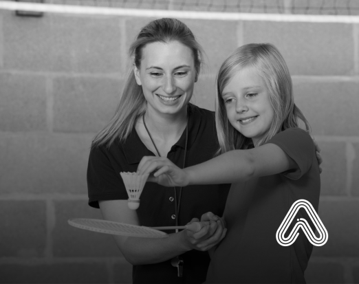 PE teacher helping girl to play badminton