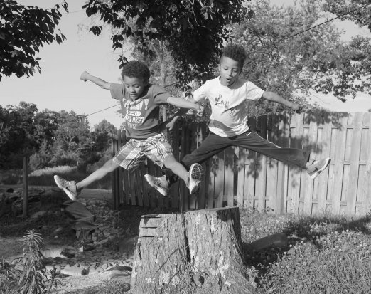 Two Young Boys Leaping Off a Tree Stump
