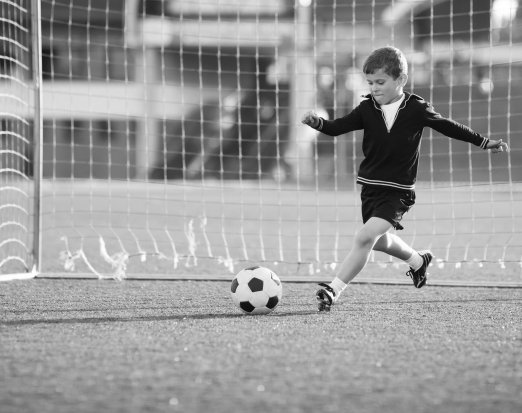Young Boy Standing in Goal & Kicking a Football