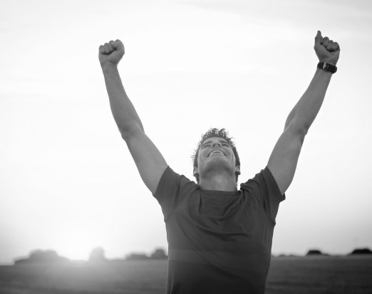 Man in red t shirt celebrating with his arms in the air in front of sunset