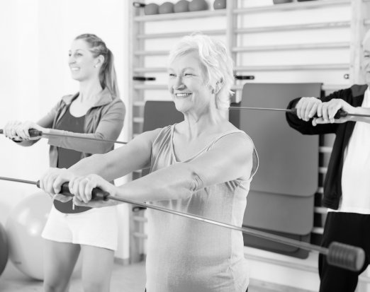 Group of older people and young girl exercising with barbell in gym