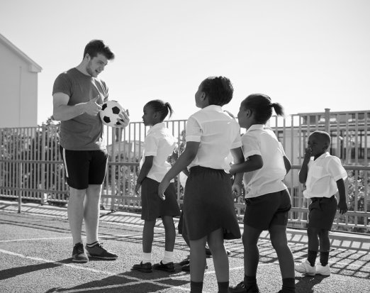 Teacher stood with group of girls and football